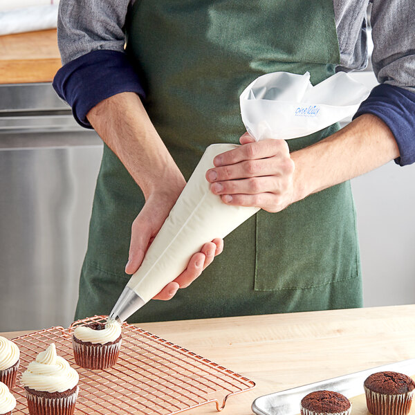 A person in a green apron using an Enjay clear disposable pastry bag to frost a cupcake.