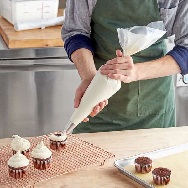 A person decorating a cupcake with a Enjay clear disposable pastry bag.