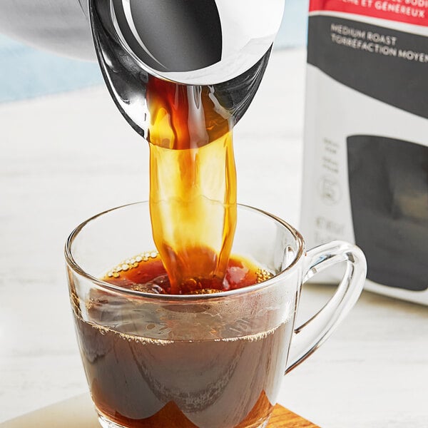 A glass cup of Lavazza Classico ground coffee with cream being poured into it.