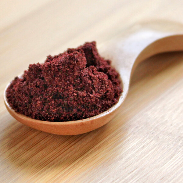 A wooden spoon filled with blackberry powder.