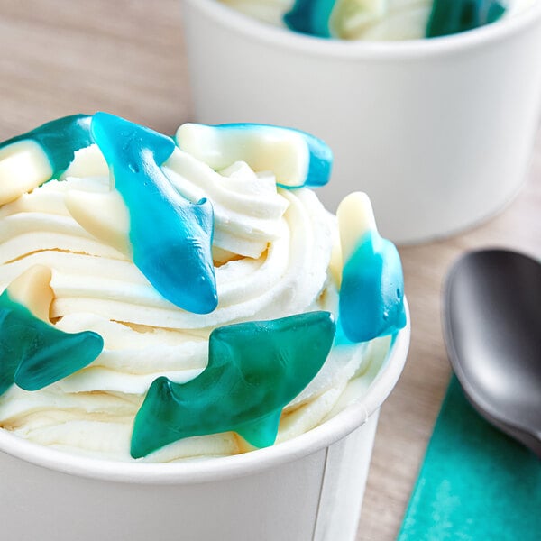 A cup of ice cream with blue and white Albanese gummy sharks.