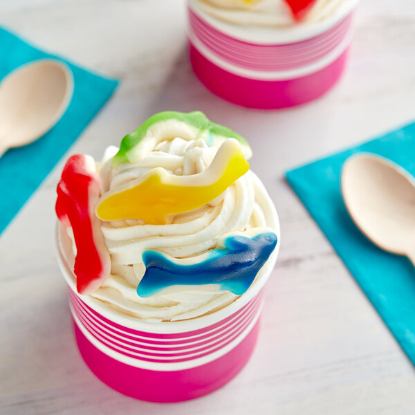 A pink and white cup of ice cream with Kervan assorted colored gummy sharks on top.