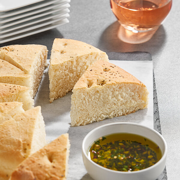 A piece of Turano Italian Herb Focaccia bread on a plate with a bowl of sauce.