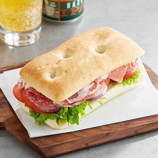 A sandwich with meat and vegetables on a Turano Sliced Potato Focaccia roll on a wooden board.