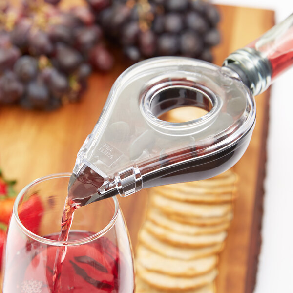 A person using a Vacu Vin wine aerator to pour red wine into a glass.