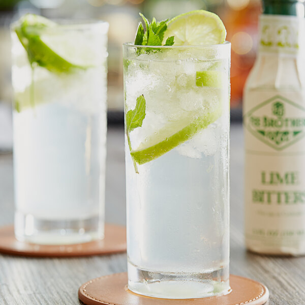 A glass of water with lime slices and mint leaves with a bottle of Fee Brothers Lime Bitters.