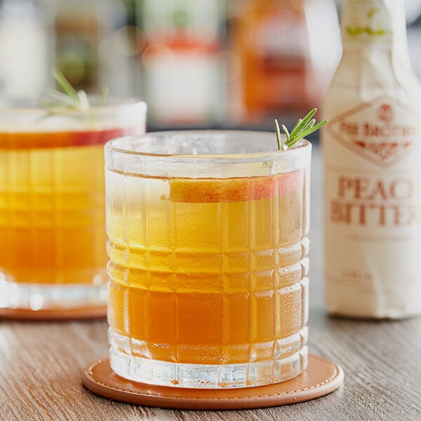 Two glasses of a peach-flavored cocktail made with Fee Brothers Peach Bitters on a coaster.