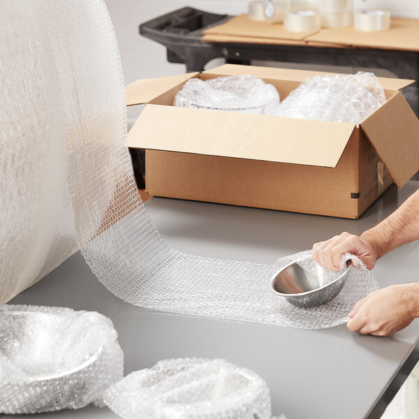 A person wrapping a silver bowl with Pregis bubble wrap on a counter.