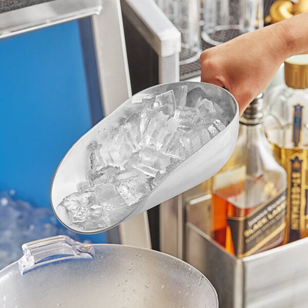 A hand holding a Choice aluminum scoop of ice over a glass.