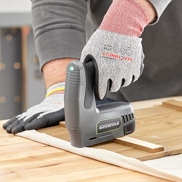 A gloved hand using a grey Genesis cordless electric stapler/nailer.