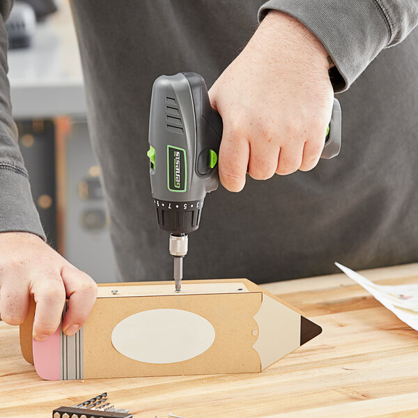 A person using a Genesis cordless screwdriver to drill a piece of wood.