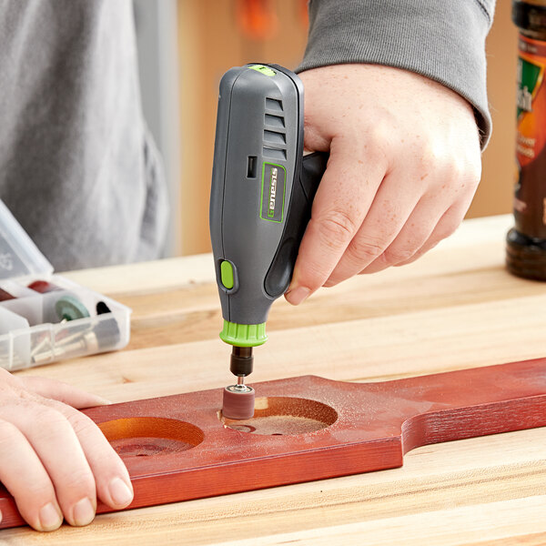 A person using a Genesis 8V Lithium-ion rotary tool to drill holes in a wooden board.