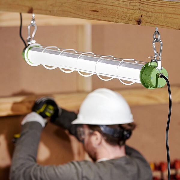 A man wearing a hard hat and goggles working on a white PowerSmith LED tube light.
