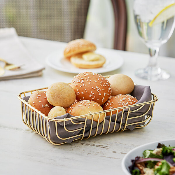 An Acopa rectangular gold wire basket filled with bread and rolls on a table.