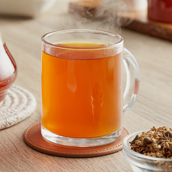 A glass mug of Davidson's Organic Pumpkin Spice Herbal tea with steam coming out of it.