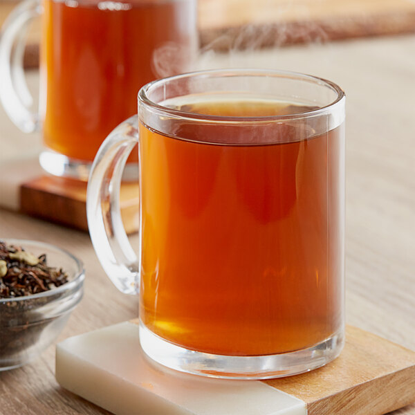 A glass mug of brown Davidson's Organic Green Chai with Orange Peel tea on a wooden surface.