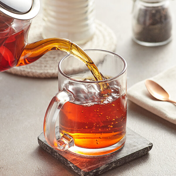 A glass teapot pouring Davidson's Organic Mountain Copper Oolong tea into a glass cup.