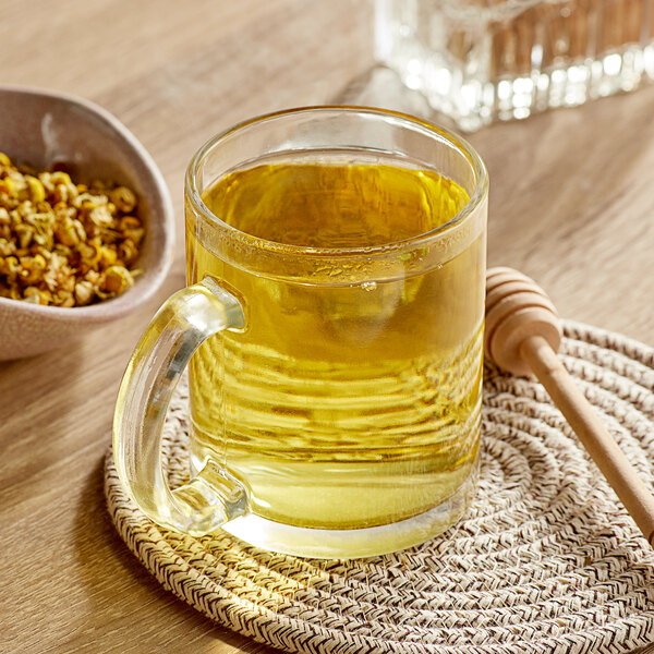 A glass mug of Davidson's Organic Chamomile Tea with loose leaf flowers on the table.
