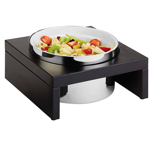 An APS Bridge cooling bowl with fruit on a black stand.