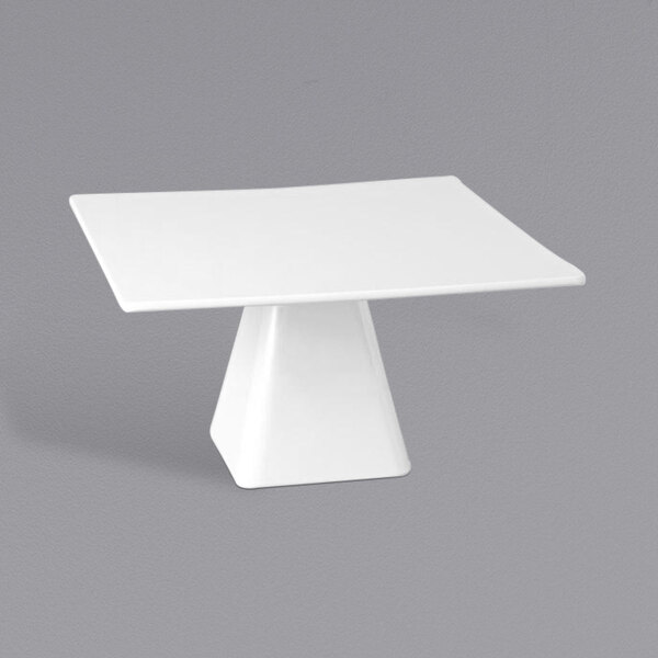 A white square tall melamine cake stand with a pedestal on a white table.