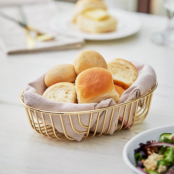 An Acopa oval gold wire basket filled with bread on a table.