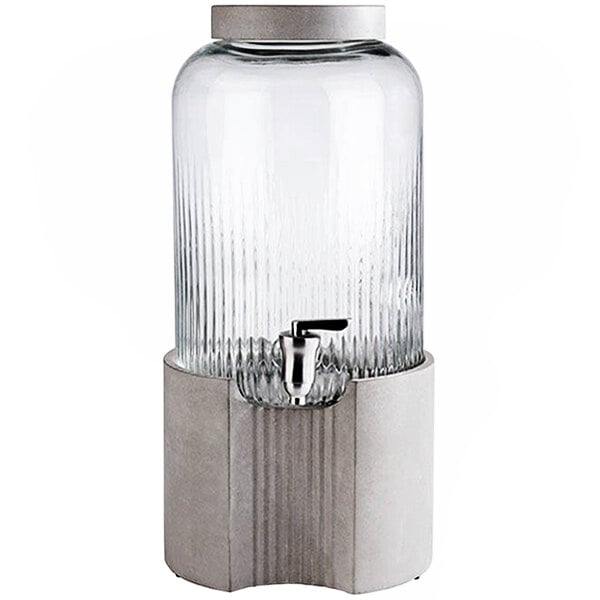 An APS Element glass drink dispenser with a silver faucet on a metal stand.