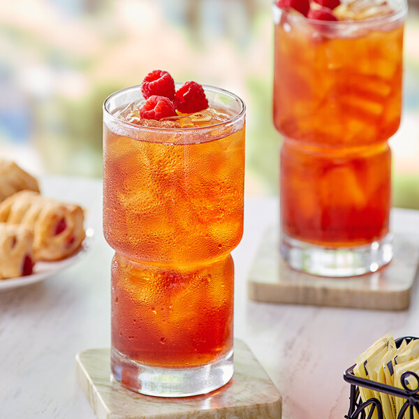 A glass of Davidson's Organic Raspberry Iced Tea with raspberries on a table.