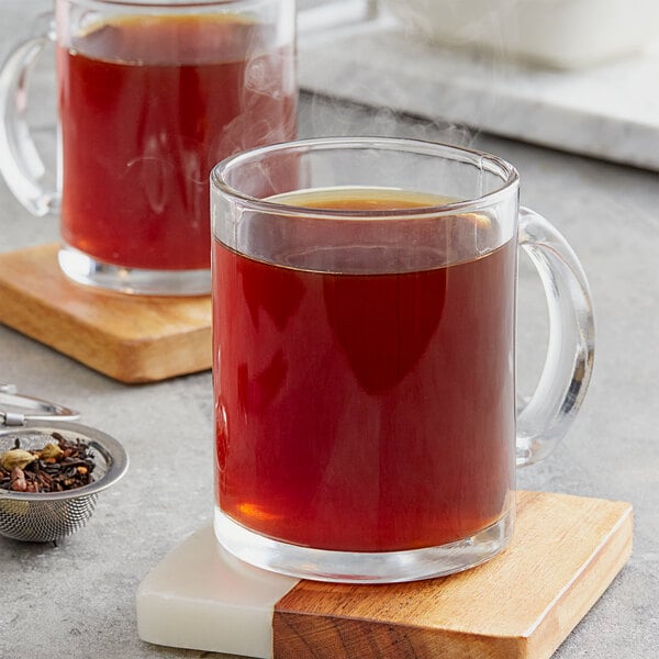 A glass mug of brown Davidson's Organic Classic Chai tea with a strainer of spices.