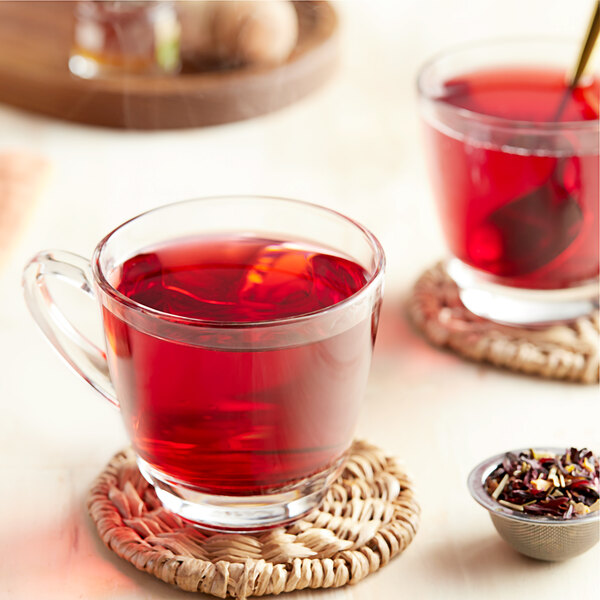 A glass mug of Davidson's Organic Te De Hibiscus tea with red liquid and a spoon.