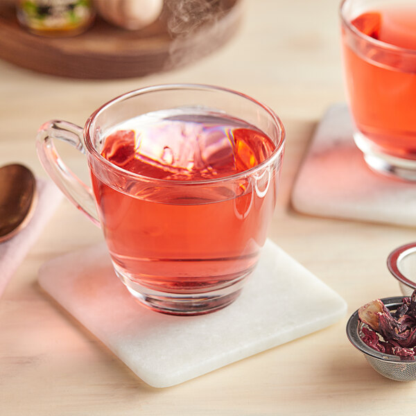 A glass mug of pink Davidson's Organic Hibiscus Tea on a white marble coaster.