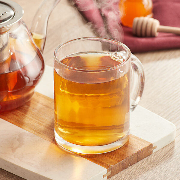 A glass mug of Davidson's Organic Himalayan White Tea on a cutting board with a wooden stick with honey.