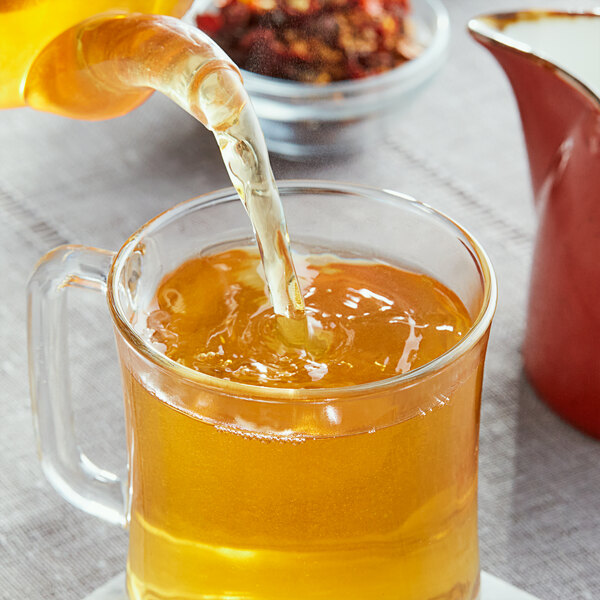A person pours Davidson's Organic Orange Spice Herbal tea into a glass.