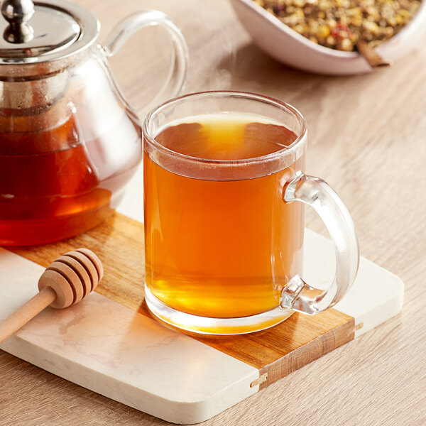 A glass mug of Davidson's Organic Chamomile and Fruit Herbal Loose Leaf Tea with a wooden spoon and honey dipper.