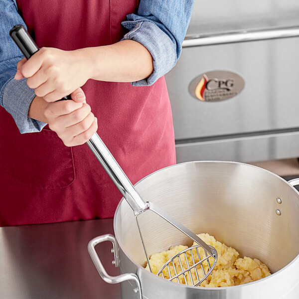 A woman using a Tablecraft round-faced potato masher to mash potatoes in a pot.