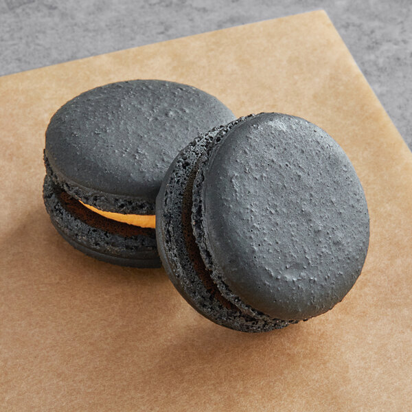 Two black Macaron Centrale with yellow filling on a brown surface.