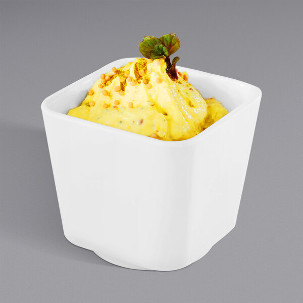 A white APS tall square melamine bowl with yellow food in it.