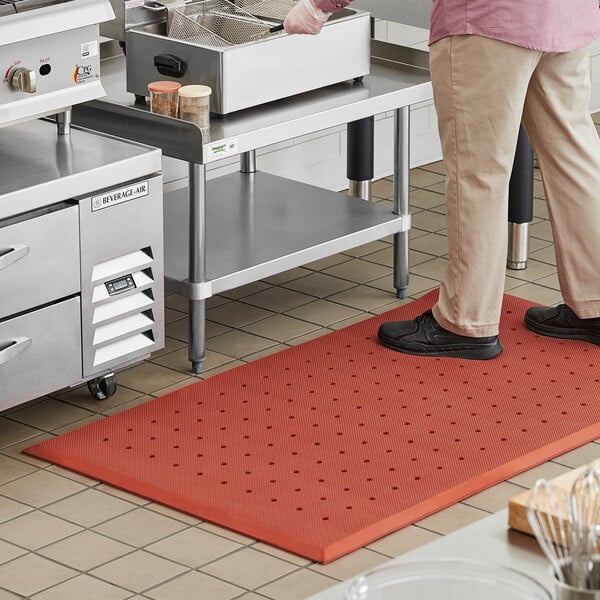 A person standing on a red Choice anti-fatigue floor mat in a kitchen.
