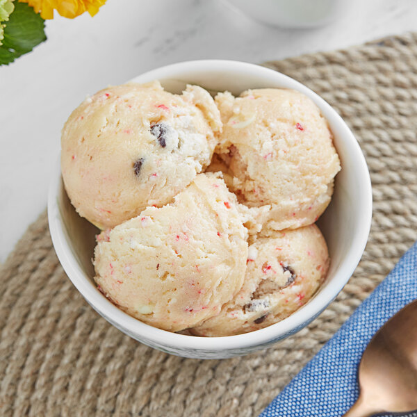 A spoon scooping Cookie Dough Bliss peppermint bark cookie dough over a bowl of ice cream.