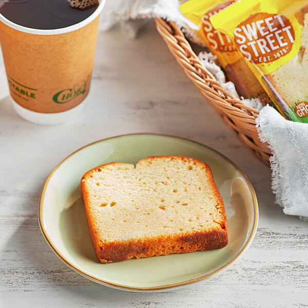 A slice of Sweet Street Lemon Pullman Loaf Cake on a plate next to a cup of coffee.