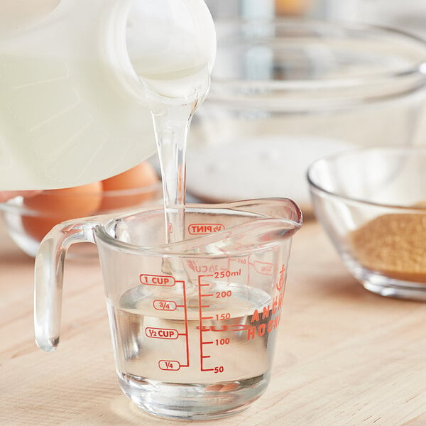 A person pours Karo Light Corn Syrup from a jug into a glass measuring cup with milk and eggs.