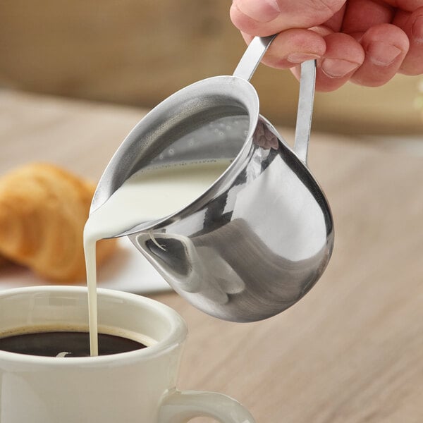 A person using a Choice stainless steel bell creamer to pour milk into a cup of coffee.