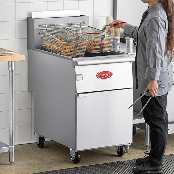A woman standing next to a large Avantco natural gas floor fryer.