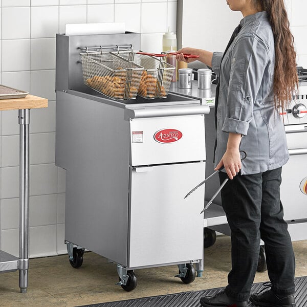 A woman standing in a professional kitchen with an Avantco stainless steel floor fryer.