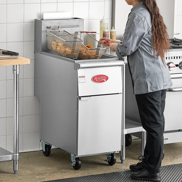 A woman standing in front of an Avantco stainless steel floor gas fryer.