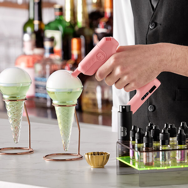A person holding a pink Flavour Blaster over ice cream cones in glass cones.