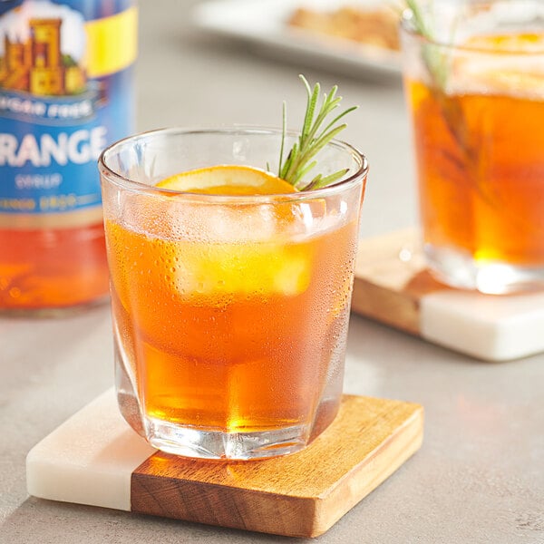 A glass of Torani sugar-free orange liquid with a slice of lemon and rosemary.