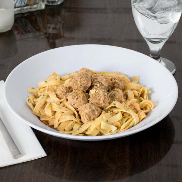 A white Siciliano bowl filled with pasta and meatballs on a table.