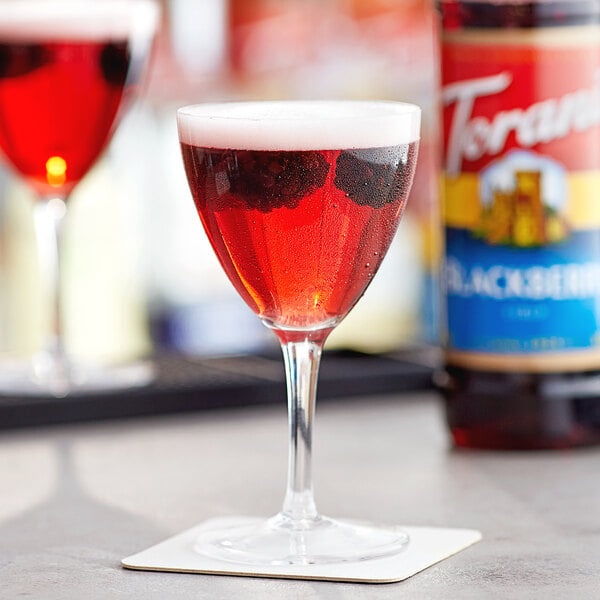 A red wine glass filled with Torani blackberry flavored liquid on a table.