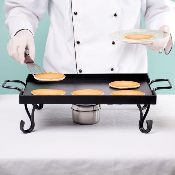 A chef using an American Metalcraft wrought iron griddle to cook pancakes.