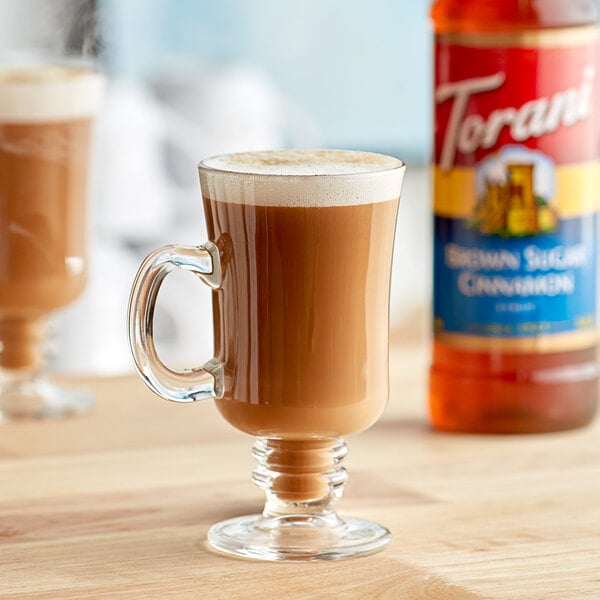 A glass cup of brown coffee next to a bottle of Torani Brown Sugar Cinnamon flavoring syrup.